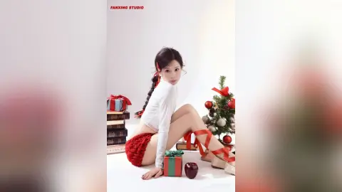 Young woman in white long-sleeve top and red knit shorts sitting by a Christmas tree with festive gift boxes.