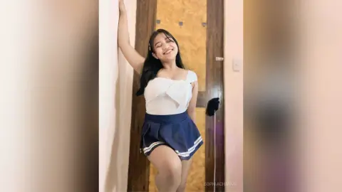Happy young woman in a white top and navy blue skirt leaning against a doorway in a bright indoor setting.