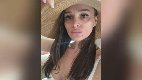Beautiful woman in a white summer outfit and wide-brimmed straw hat posing for a sunny outdoor selfie.