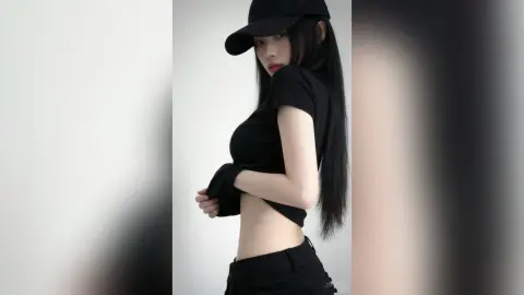 ZhiYue poses in a black cap and short-sleeved black crop top, showing her long black hair and midriff against a plain white background.