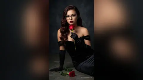 Elegant woman in black velvet dress and long gloves holding a red rose against a dark moody background.