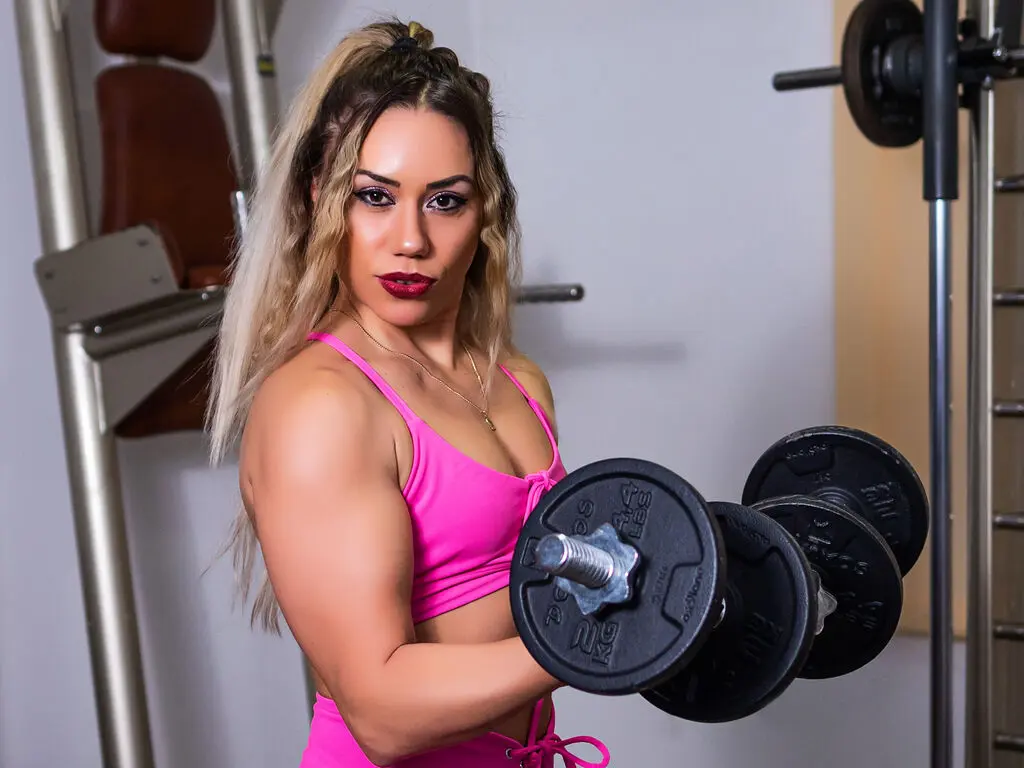 Athletic woman in pink sports bra lifting a heavy dumbbell in a gym setting with a focused mood.