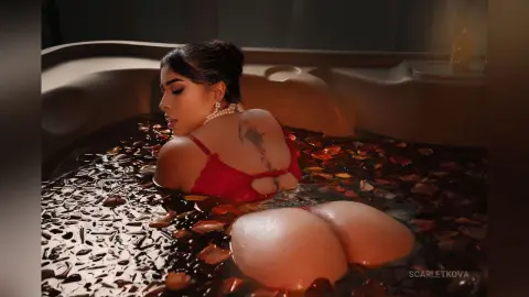 Woman in red bikini relaxing in a luxury bubble bath filled with red rose petals for a romantic mood.