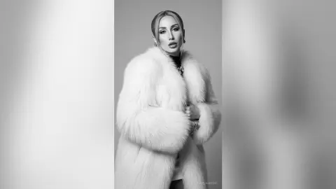 Elegant woman in a luxurious white faux fur coat posing in a sophisticated black and white studio portrait.