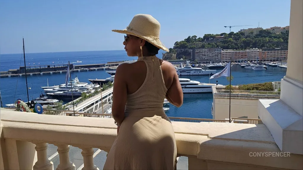 ConySpencer β ConySpencer wears a tan halter dress and a sun hat while looking out over a Mediterranean harbor filled with yachts.