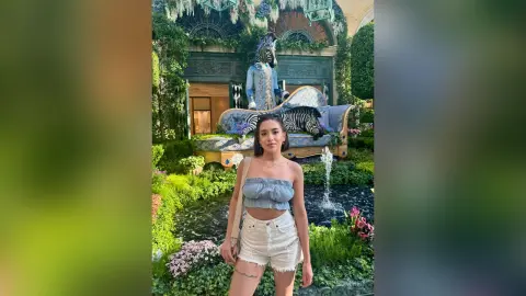 Young woman in a blue tube top and white denim shorts posing in a lush garden with whimsical zebra statues.