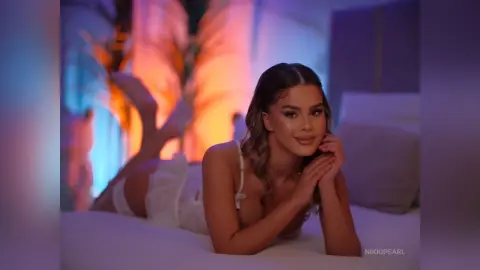 Young woman in white loungewear relaxing on a bed with warm, moody ambient lighting.