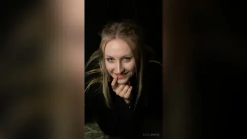 Smiling blonde woman in a black outfit posing against a dark background for a moody portrait.