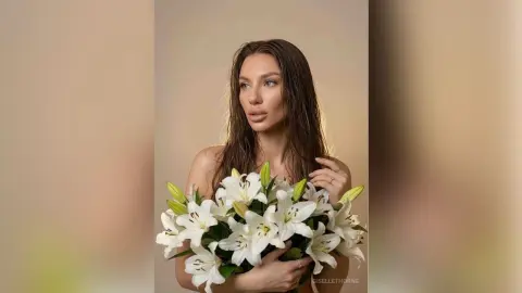 Elegant woman with wet hair holding a large bouquet of white lilies in a soft, minimalist studio setting.