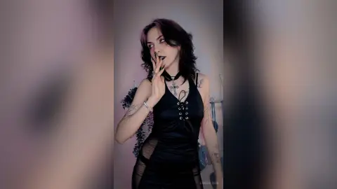 LorenLoiss poses in a black lace-up tank top, looking off-camera with dark lipstick and wavy dark hair.
