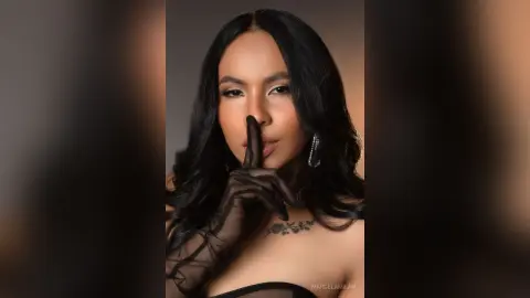 Elegant woman in black lace gloves and dark makeup posing with a mysterious expression against a dark backdrop.