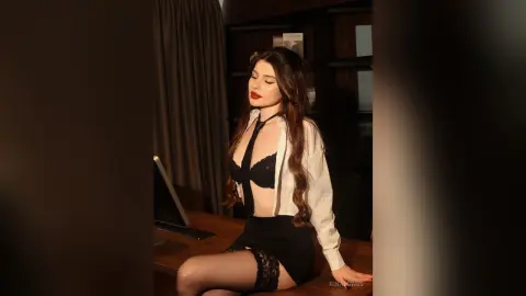 Elegant woman in white shirt and black lingerie sitting on a desk in a moody, dimly lit office setting.