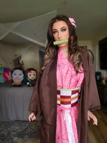 Woman in pink patterned kimono and brown robe holding a bamboo muzzle in a cozy indoor setting.