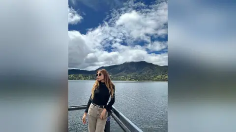 LaurentBelluci stands on a balcony overlooking a large lake, wearing a black long-sleeved top and light-colored trousers.