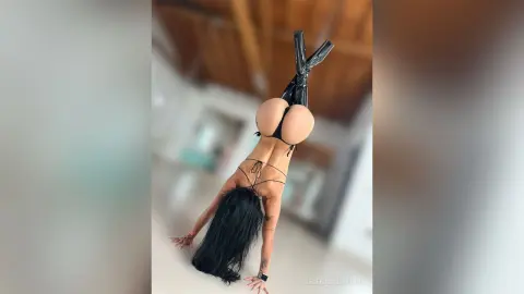 Fit woman in black lingerie performing a handstand in a bright, modern minimalist room.