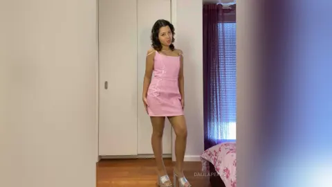 DalilaPearl — DalilaPearl stands in a pink shiny mini dress and silver high heels in a bedroom.