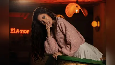 Smiling woman in a cozy pink sweater leaning on a bar in a warm, dimly lit restaurant setting.