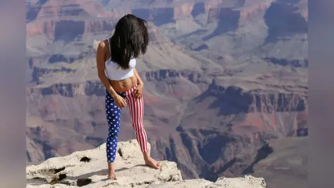 Young woman in patriotic star and stripe leggings standing on a rocky Grand Canyon cliff overlooking the canyon.