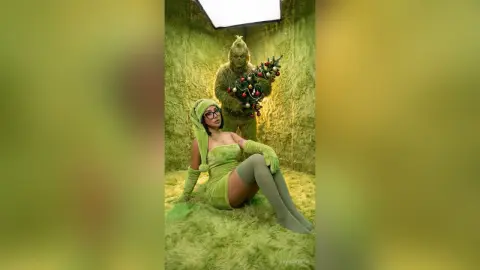Woman in green velvet outfit sitting next to Grinch character in a fuzzy green studio setting.