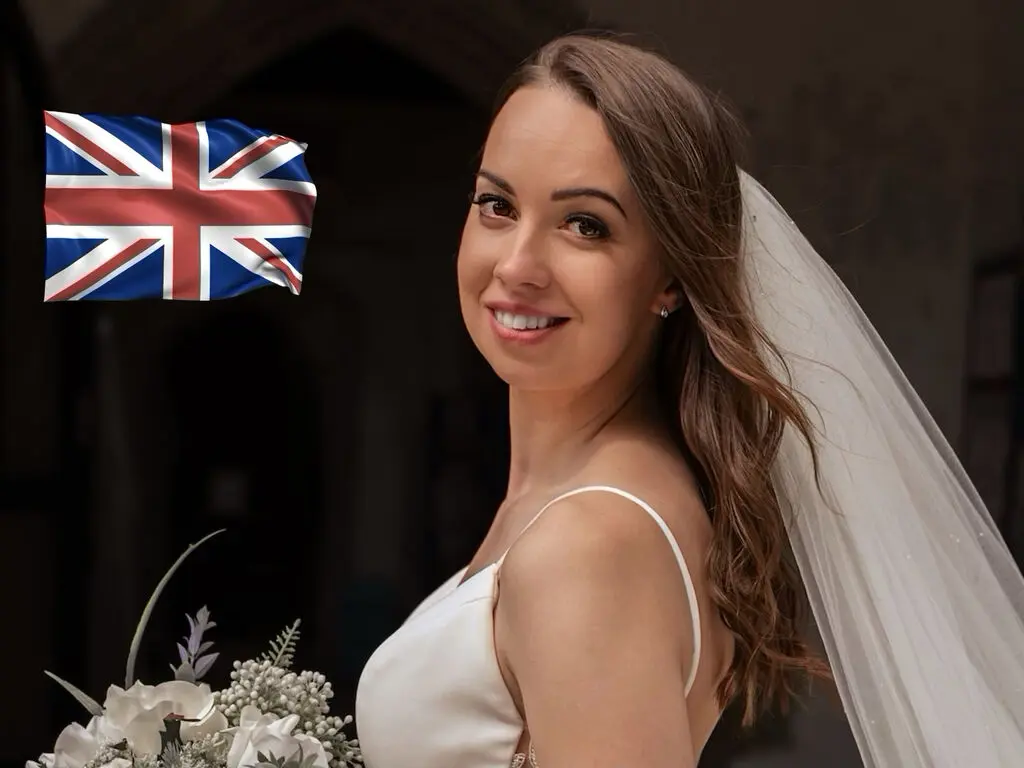 Smiling bride in a white wedding dress and veil holding a bouquet in a romantic indoor setting.