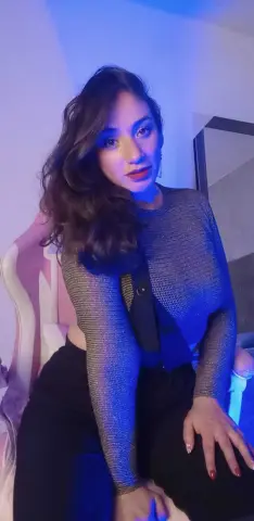 Woman in a sparkly silver mesh top and black pants sitting in moody blue lighting.