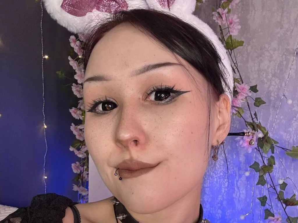 Close-up portrait of a woman with winged eyeliner and bunny ears in a dreamy, floral setting.