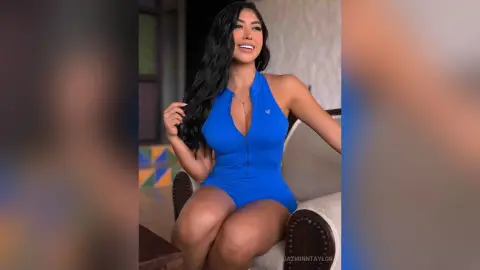 Smiling woman in a blue sleeveless bodysuit sitting on a chair in a bright indoor setting.