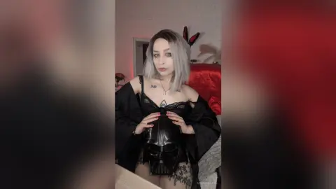 Woman with silver hair in black lace lingerie and a Darth Vader corset posing in a moody bedroom setting.