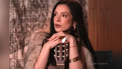 ElizabethChantal — ElizabethChantal rests her chin on her hands while posing with an acoustic guitar and wearing a fur coat.