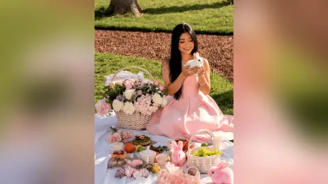 Smiling woman in a pink dress enjoying a spring picnic with flowers and bunny decorations in a sunny garden.