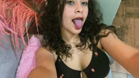 Young woman with curly hair in a black floral bralette relaxing on a pink textured sofa.