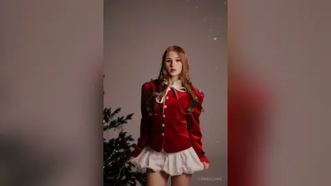 Elegant woman in a red velvet blazer and white skirt posing against a dark festive background.