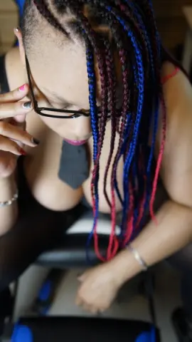 Woman with long blue and red braids wearing glasses in a relaxed indoor setting.
