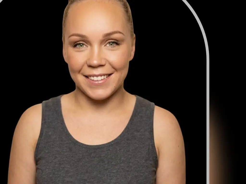 Smiling blonde woman in a grey tank top against a dark studio background.
