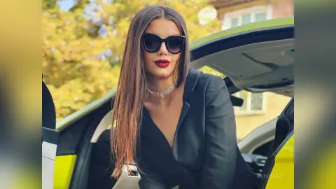 Stylish woman in a black blazer and sunglasses sitting in a lime green car on a sunny day.