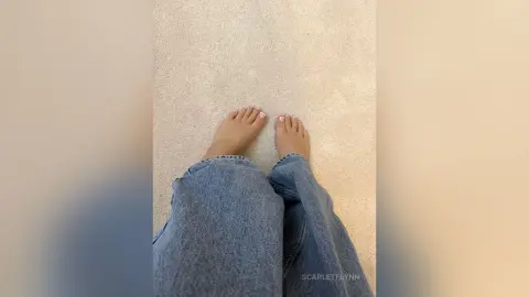 Top down view of a person wearing casual blue denim jeans and bare feet on a neutral beige floor.