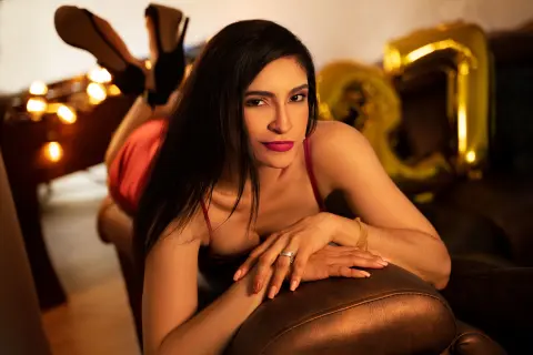Elegant woman in a red dress relaxing on a dark sofa in a warm, moody indoor setting.