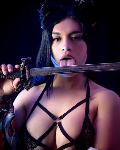 Young woman in black lace lingerie holding a silver sword with a playful expression in moody lighting.
