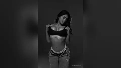 Young woman in black Calvin Klein sports bra and denim jeans posing in a moody black and white studio portrait.