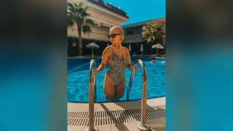 Blonde woman in a zebra print swimsuit posing by a sunny outdoor swimming pool on a summer vacation.