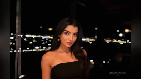 Elegant woman in a black strapless dress posing against a blurred night cityscape background.