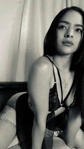 Young woman in black lace lingerie posing thoughtfully in a moody, black and white indoor setting.