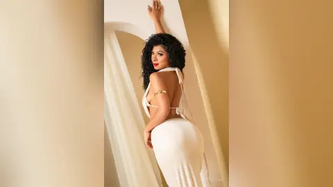 Elegant woman in a white backless evening gown posing against a minimalist cream backdrop with a sophisticated mood.