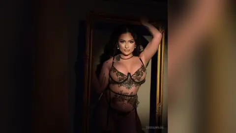 Glamorous woman in black lace lingerie posing confidently in a gold mirror under moody lighting.