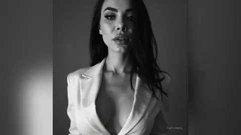 Moody black and white portrait of a brunette woman in a white blazer looking into the camera.