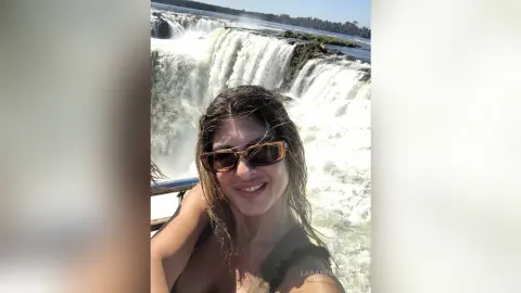 Smiling woman in sunglasses enjoying a sunny day at a massive white waterfall landscape.