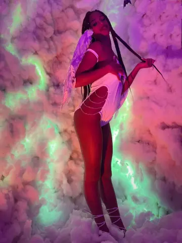 Woman in white angel wings and bodysuit posing amidst dreamy pink and green neon clouds.