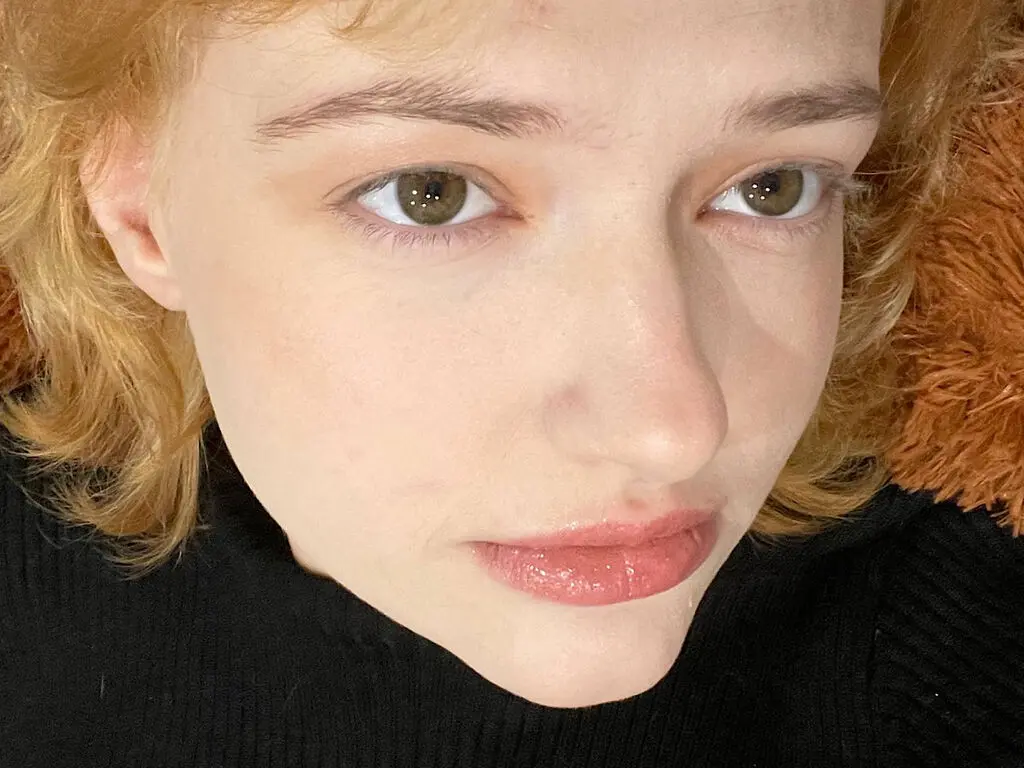Close-up portrait of a fair-skinned woman with wavy blonde hair wearing a black turtleneck sweater.