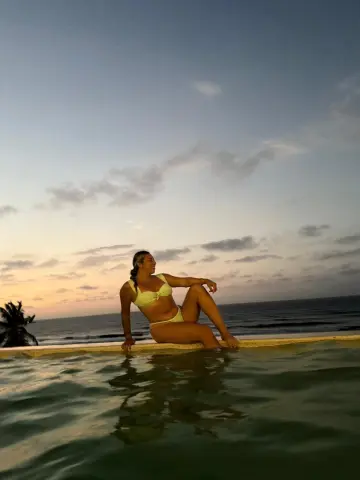 Young woman in a yellow bikini relaxing by a pool at sunset for a peaceful tropical vacation mood.