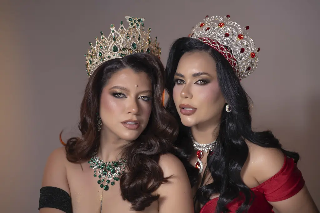 Two glamorous beauty queens in sparkling crowns and emerald jewelry posing for a luxury portrait.